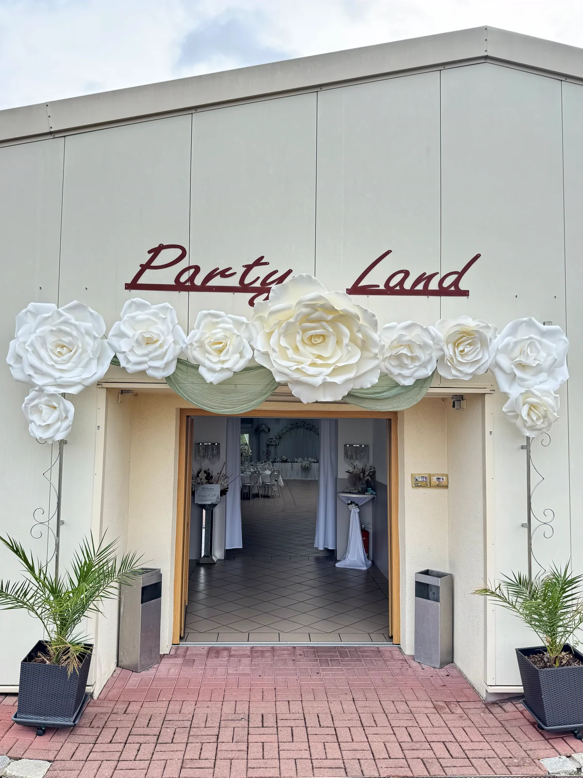 Der Eingang der Eventhalle Partyland mit großen weißen Papierrosen und dem Party-Land-Schriftzug