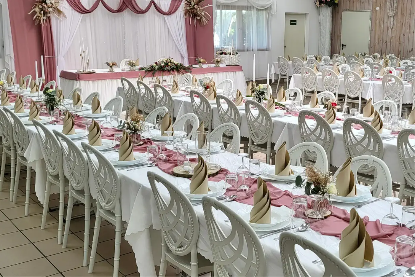 Lange Tafeln mit weißen Tischdecken, altrosa Läufern und champagnerfarbenen Servietten in der Eventhalle Partyland
